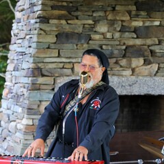 The lead singer of The GroovaLottos sings into a microphone while playing the keyboard.