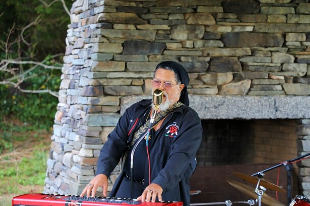 The lead singer of The GroovaLottos sings into a microphone while playing the keyboard.