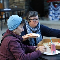 Two seated women enjoy pizza.