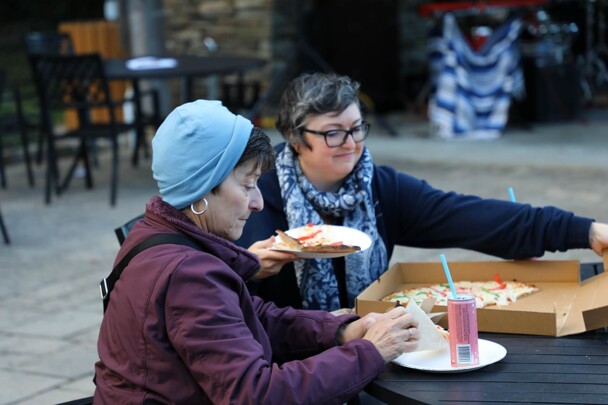 Two seated women enjoy pizza.