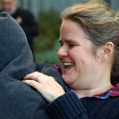 A young mother laughs as she holds her child who wears a grey hoodie.