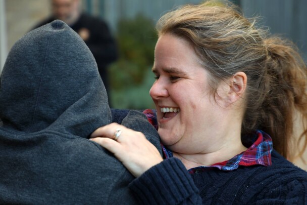 A young mother laughs as she holds her child who wears a grey hoodie.