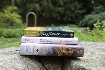 Three books stacked on a stone fragment in a garden