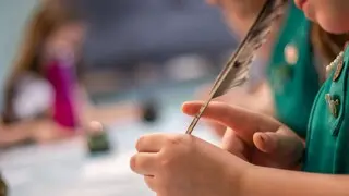 Girl scout uses quill pen to write on a piece of paper