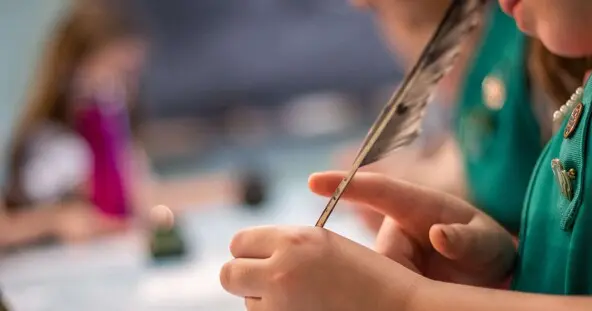 Girl scout uses quill pen to write on a piece of paper