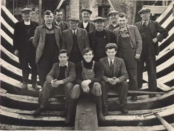 Men pose within partially constructed boat hull