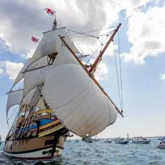 Mayflower sailing on ocean surrounded by smaller boats