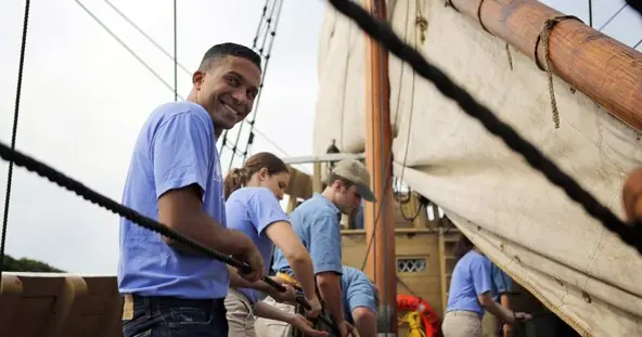 Four people work together to pull rope on deck of Mayflower
