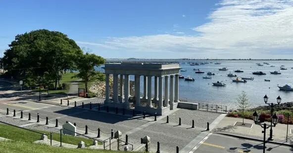 Green grass leads to Plymouth Rock Memorial and the ocean beyond