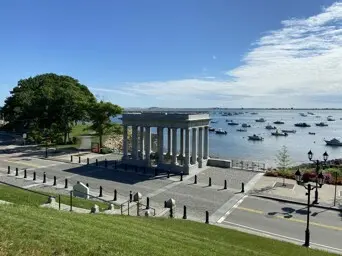 Green grass leads to Plymouth Rock Memorial and the ocean beyond