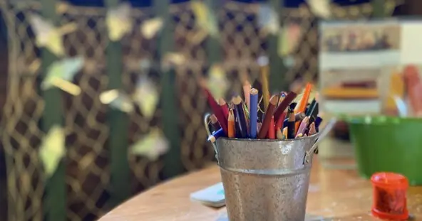 table with craft supplies including a silver bucket filled with colored pencils