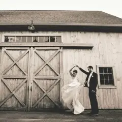 Groom spins his bride in front of a rustic barn