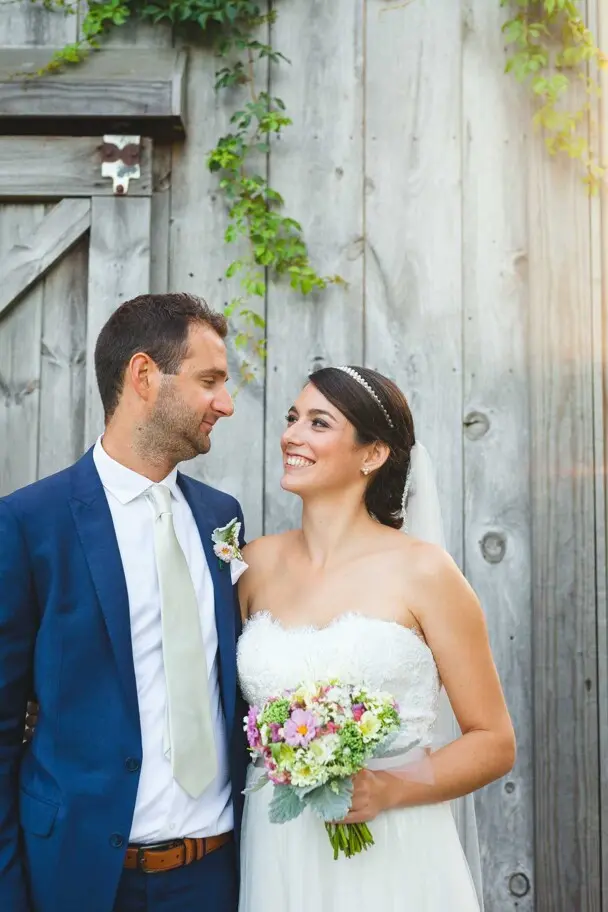 Bride and groom smile at each other in front of a barn