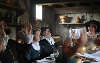 Pilgrims seated at a table pray before a meal