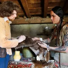 Wampanoag man and Pilgrim man inspect a fur pelt for trade.