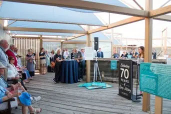 A group gathers before a speaker on the pier leading to Mayflower II